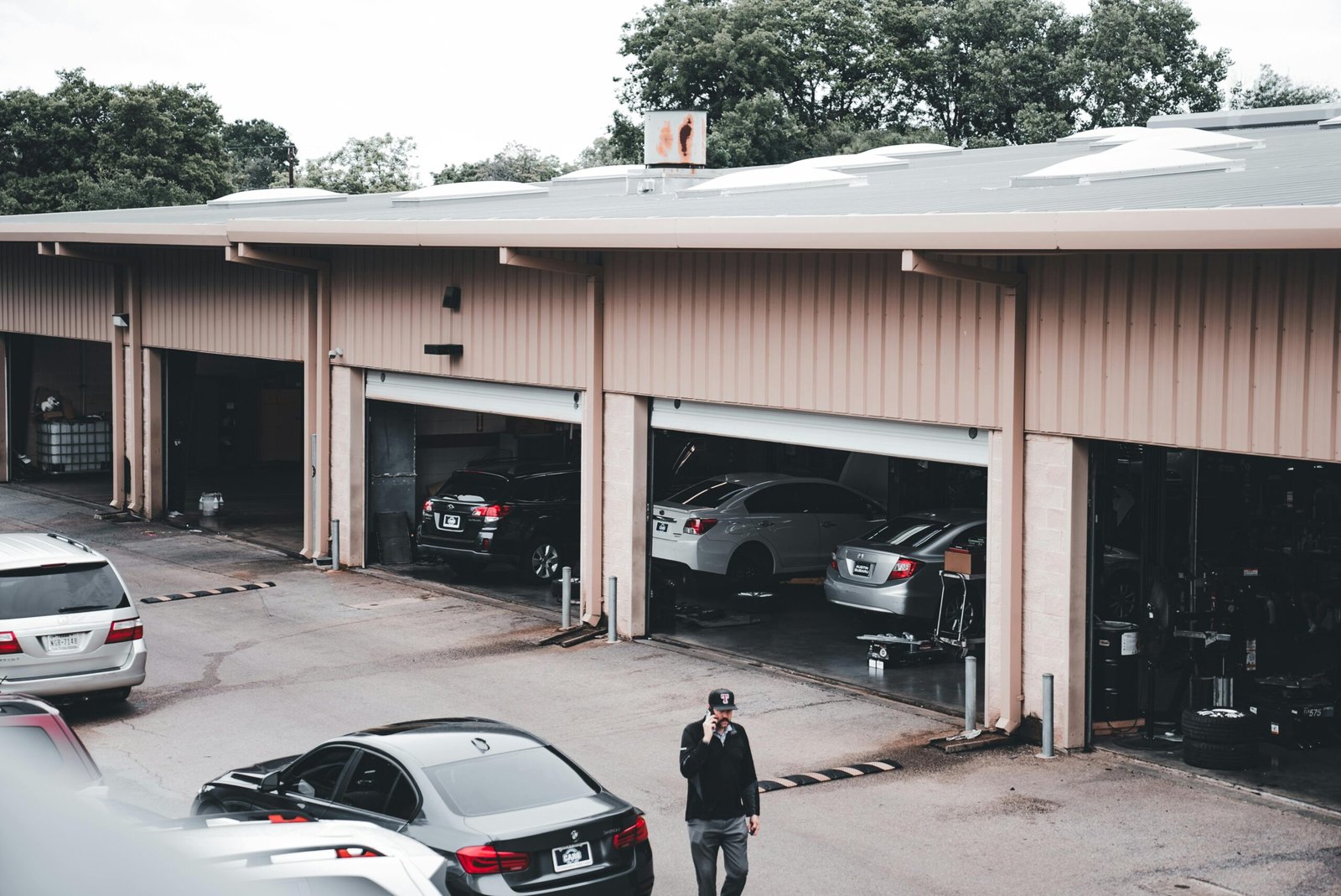 A man walks by a garage with cars parked inside and outside in an urban setting.
